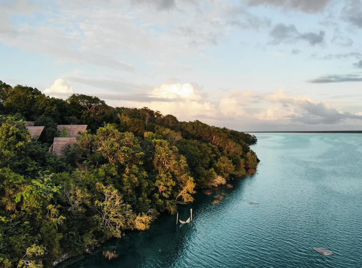 Vue aérienne de la rive de la lagune de Bacalar au coucher du soleil, avec des toits de palme dans la forêt