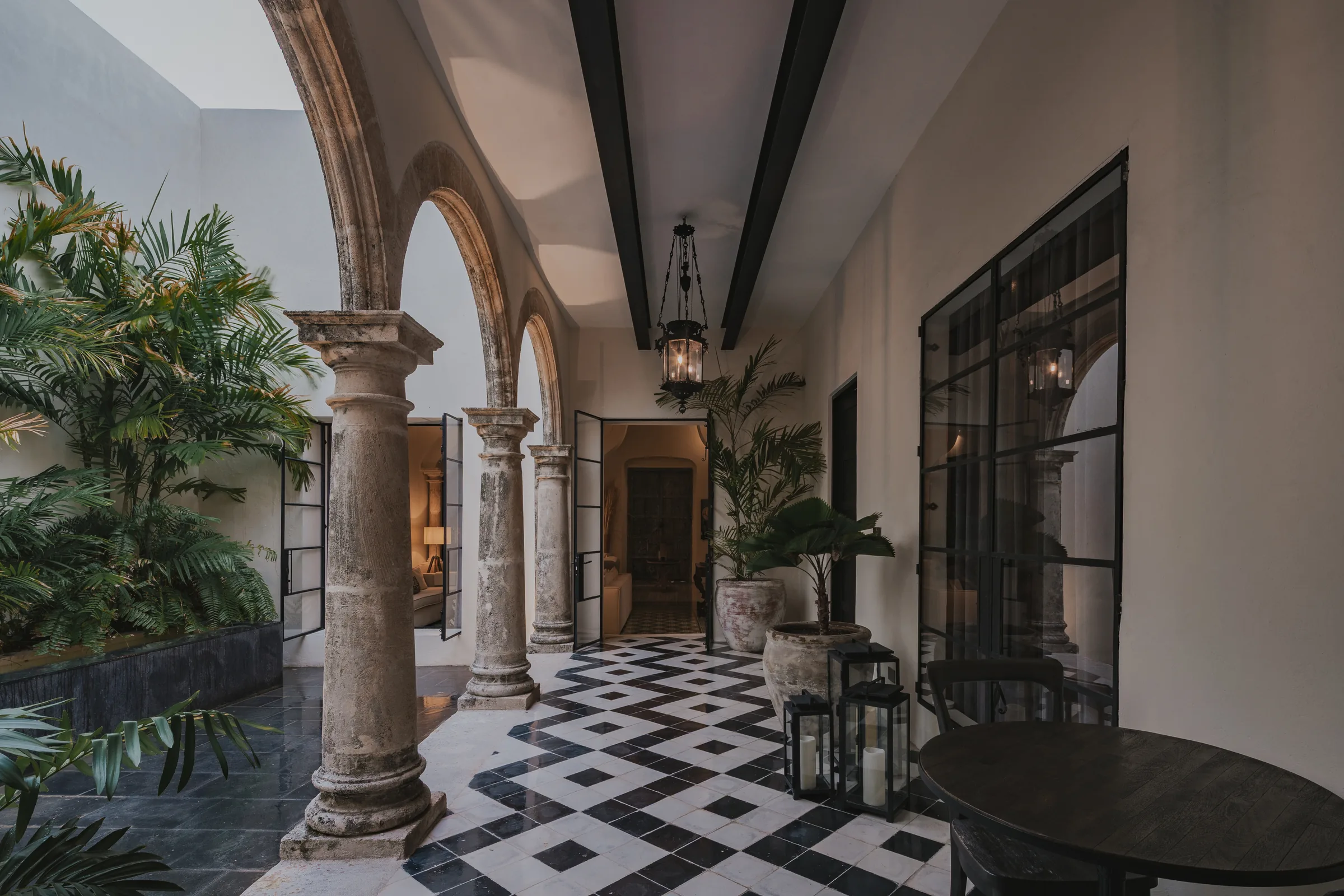 Arcade of the central courtyard at Casa Japa, with stone columns, a checkerboard pasta-tile floor and lanterns