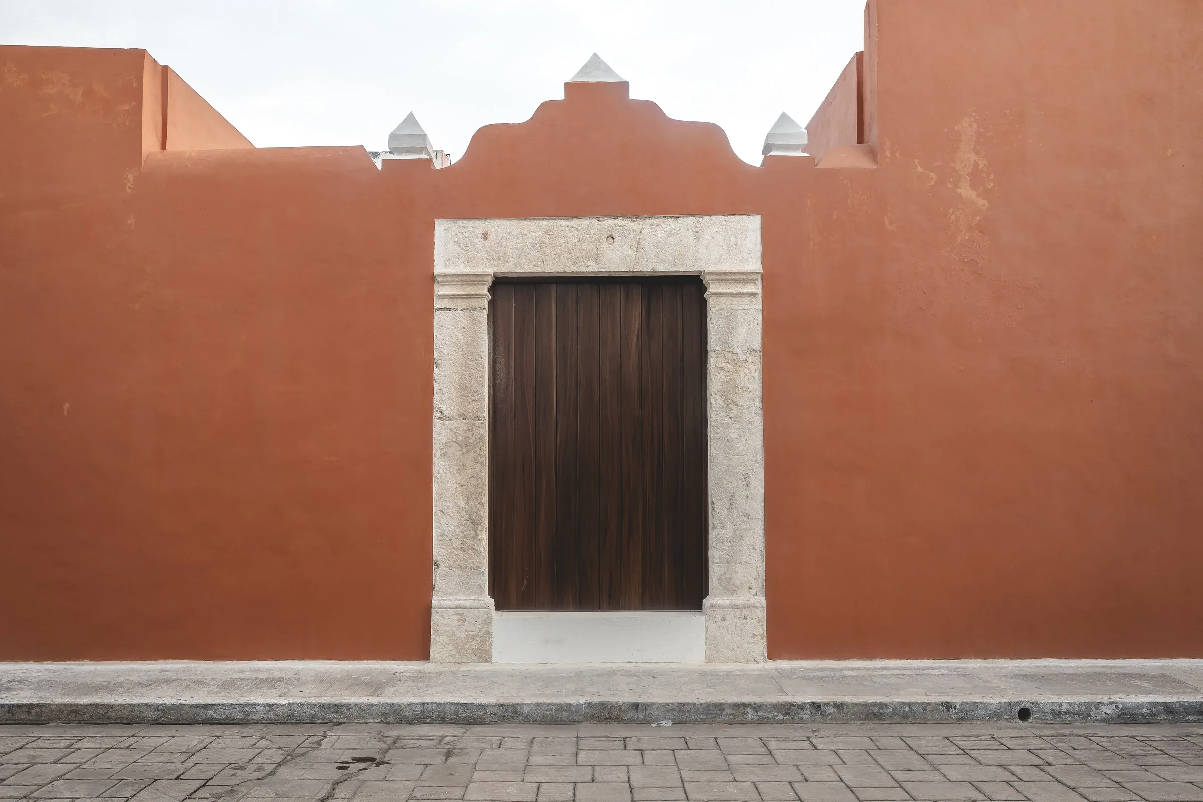 Terracotta facade of Casa Ex Templo with a curved parapet and wooden portal, in Campeche