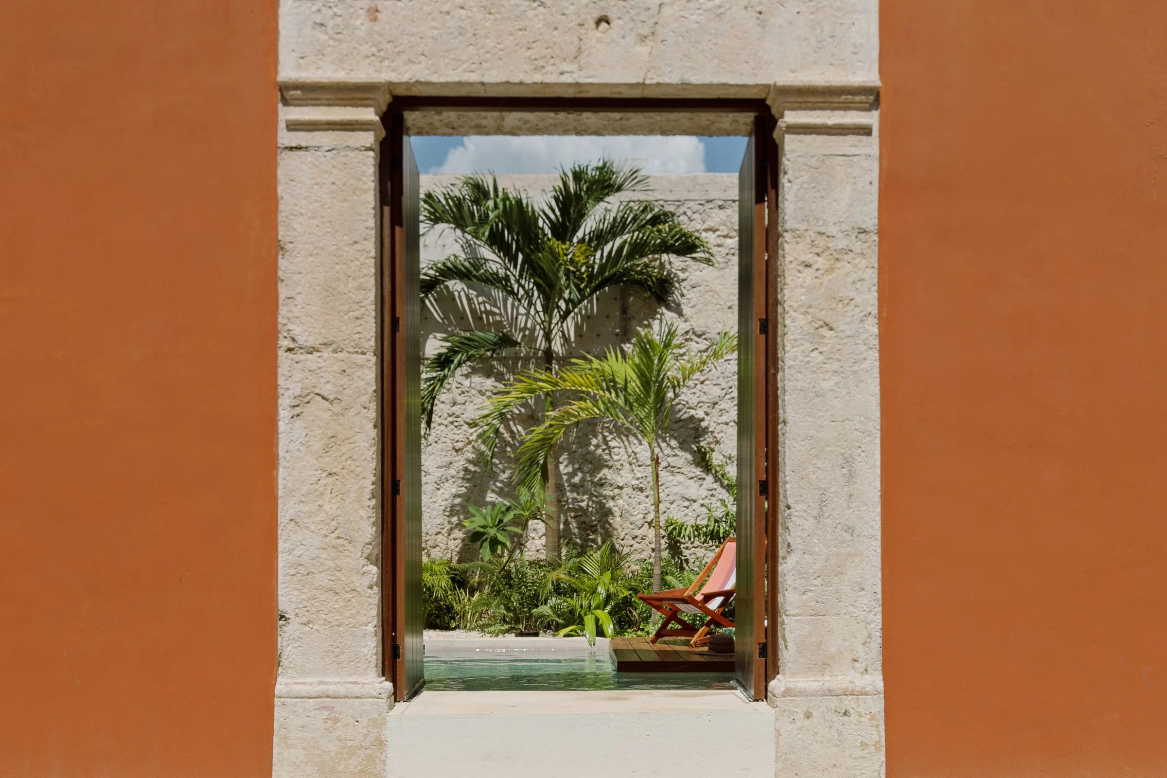 Open doorway in the terracotta facade of Casa Ex Templo, with palms and the courtyard pool beyond, in Campeche's walled city
