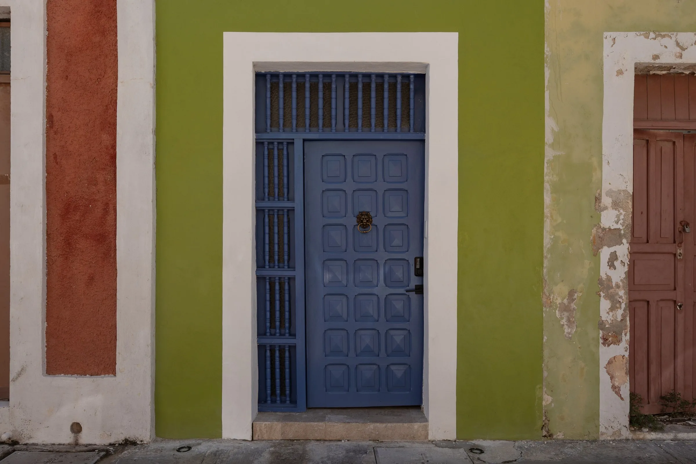 Blue door with a white frame in the green facade of Casa Pistache, Campeche