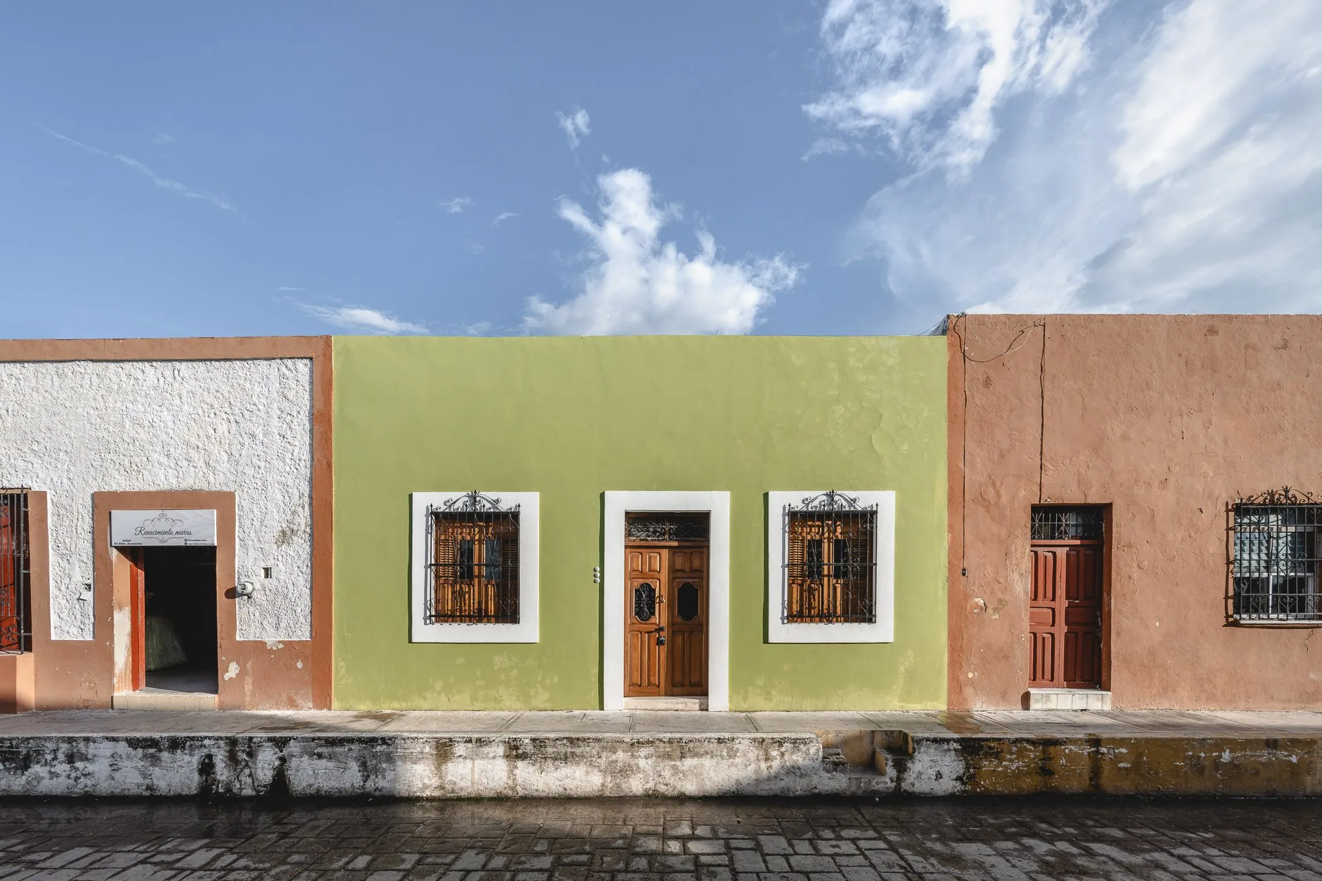 Green facade with white frames of La Casa Verde between its neighbours, in Campeche's walled city