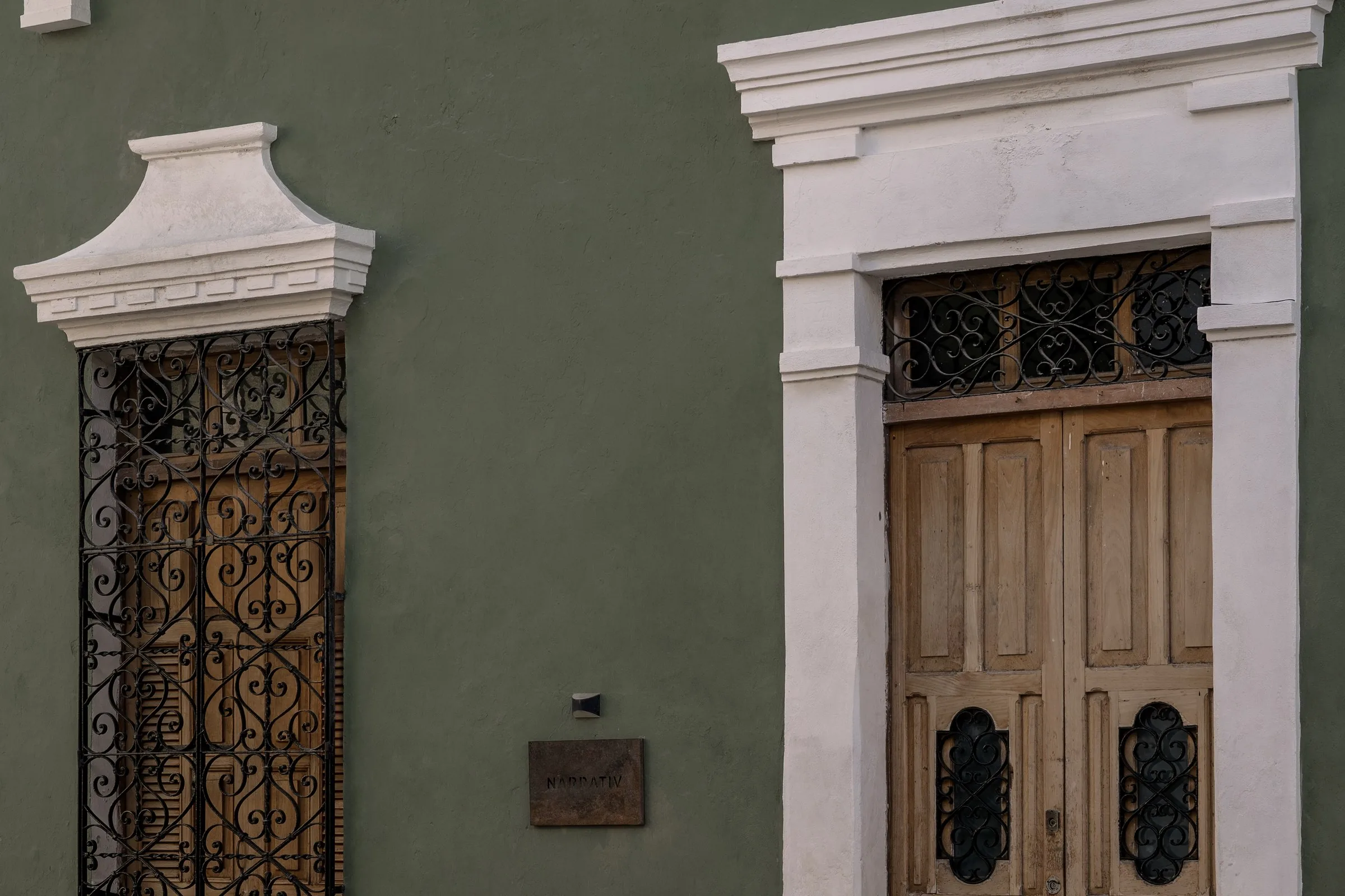Wrought-iron door and wooden door in the green facade of the Narrativ Lofts house on Calle 59, Campeche