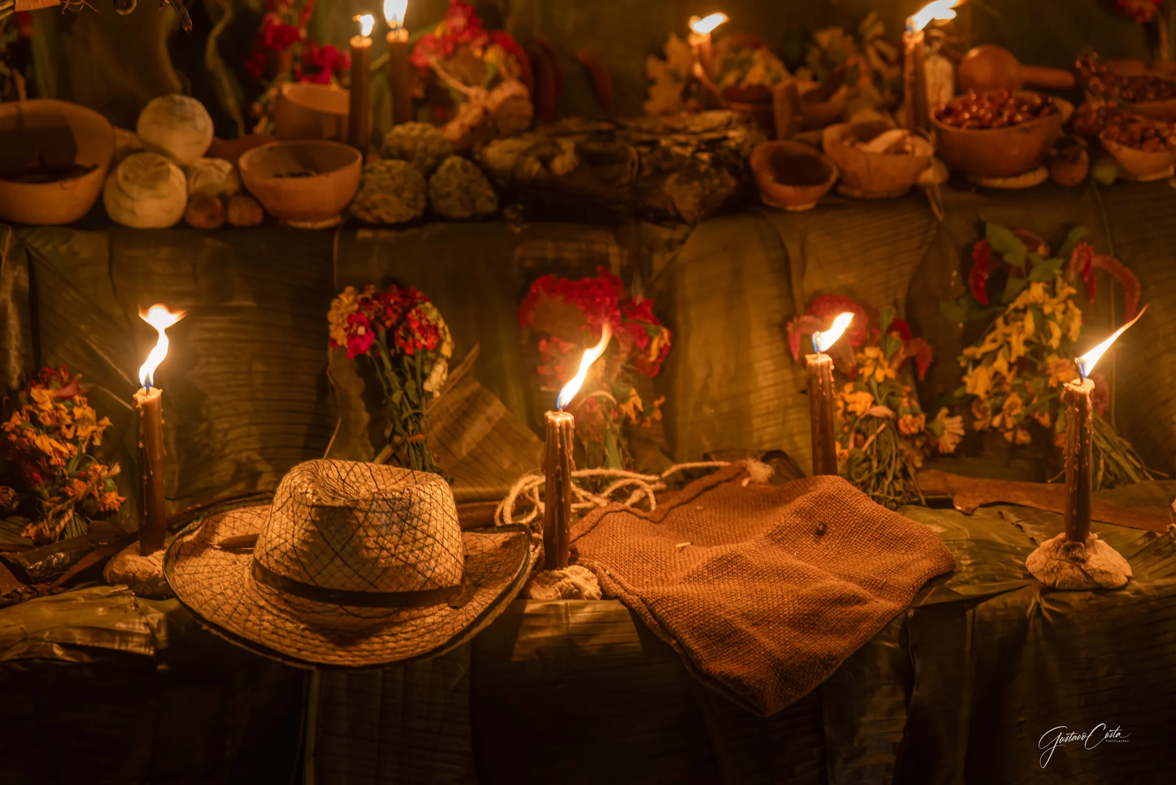 Hanal Pixán altar with lit candles, flowers, gourd bowls and a palm hat