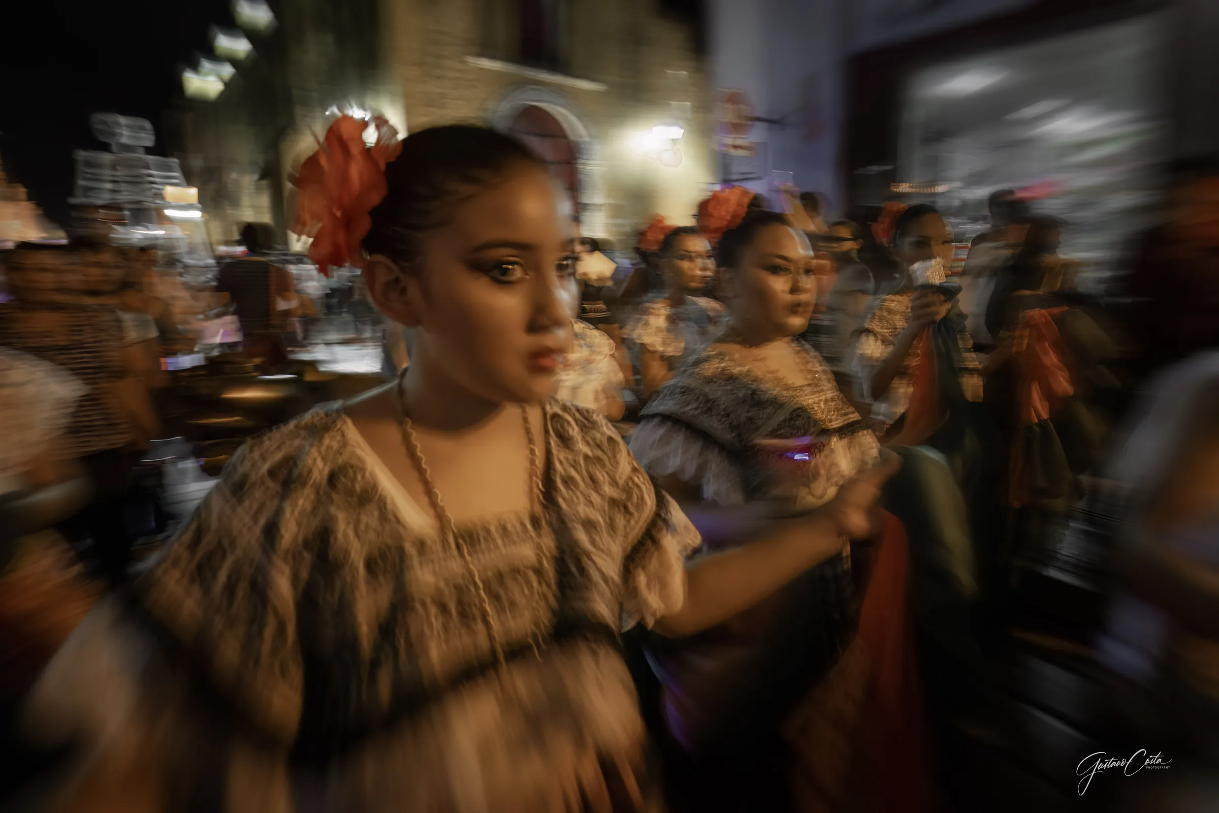Dancers in regional dress with flowers in their hair walking through a street in Campeche's historic center at night