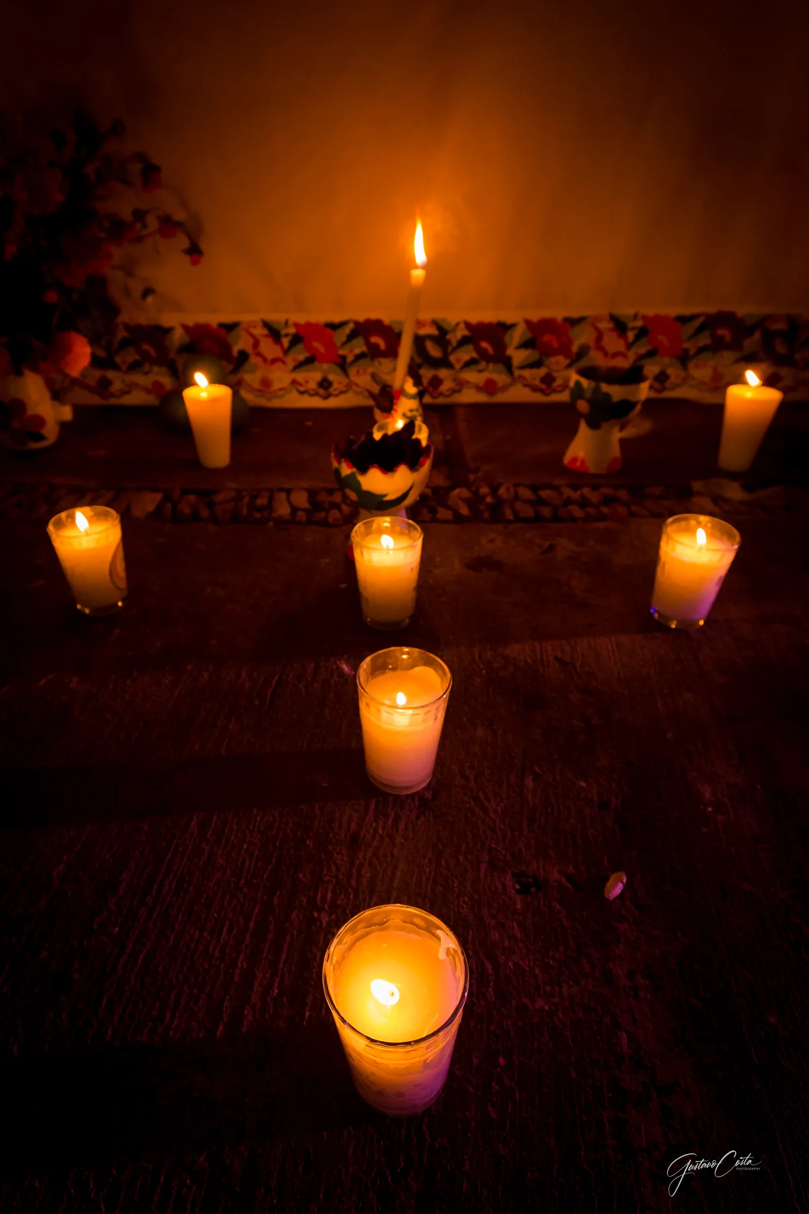 A path of lit candles on the floor leading to a small altar with flowers