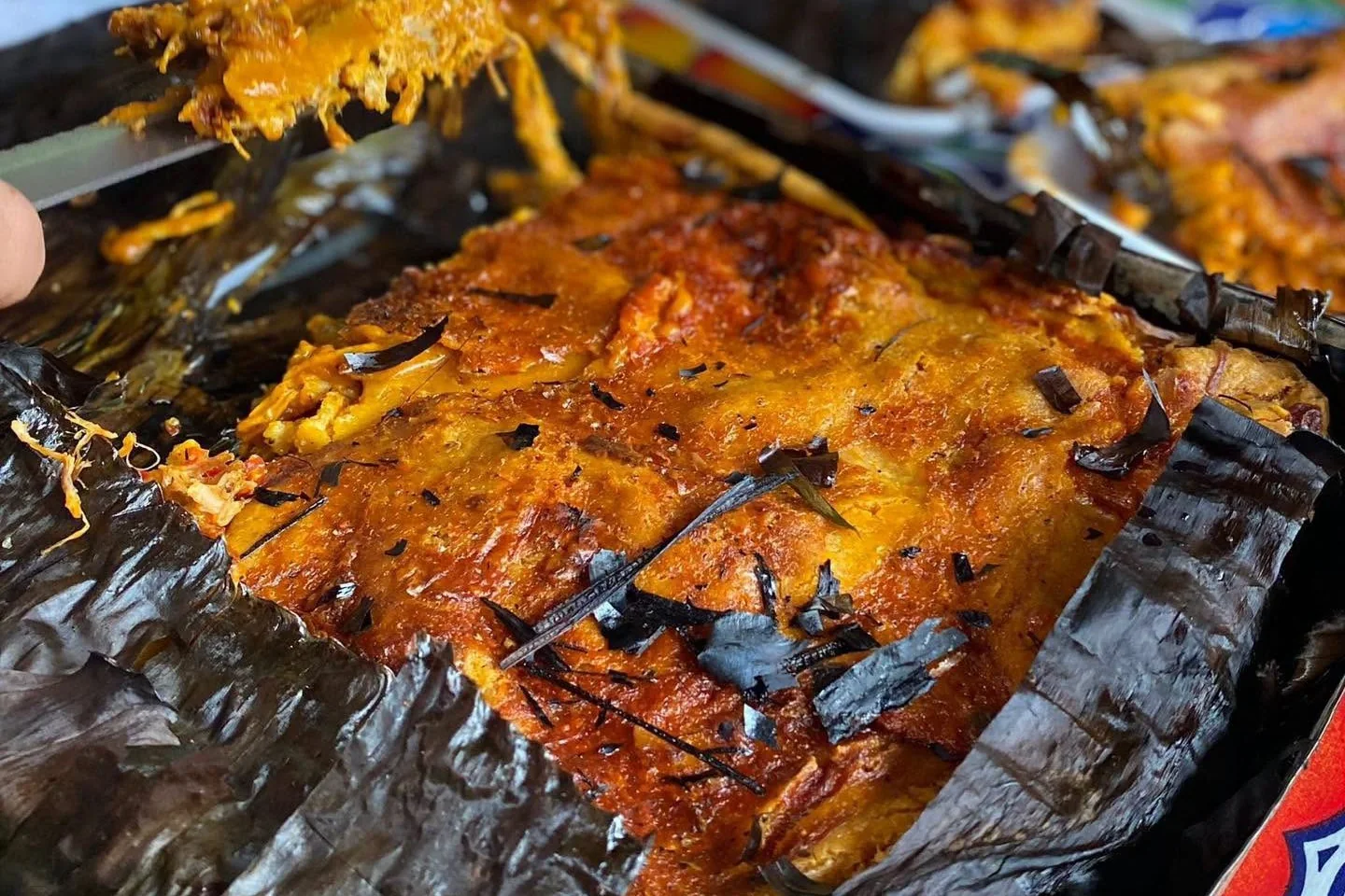 Freshly opened pibipollo in its banana leaf, with a portion being served