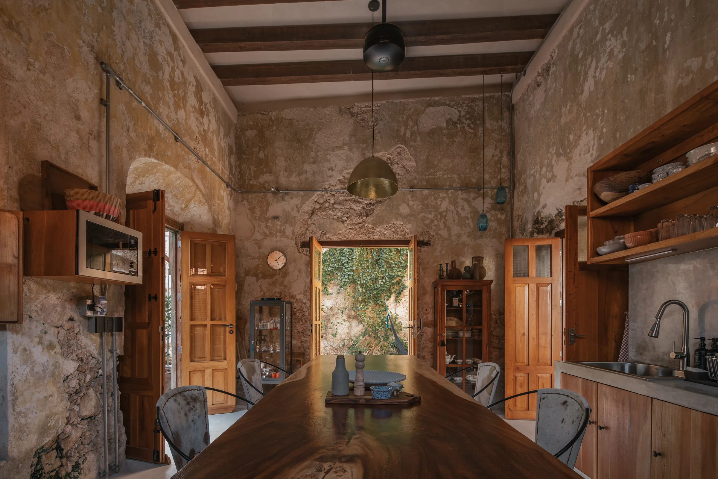 Kitchen and dining room at Casa Zotz with a long wooden table, exposed stone walls and doors open to a courtyard with climbing plants