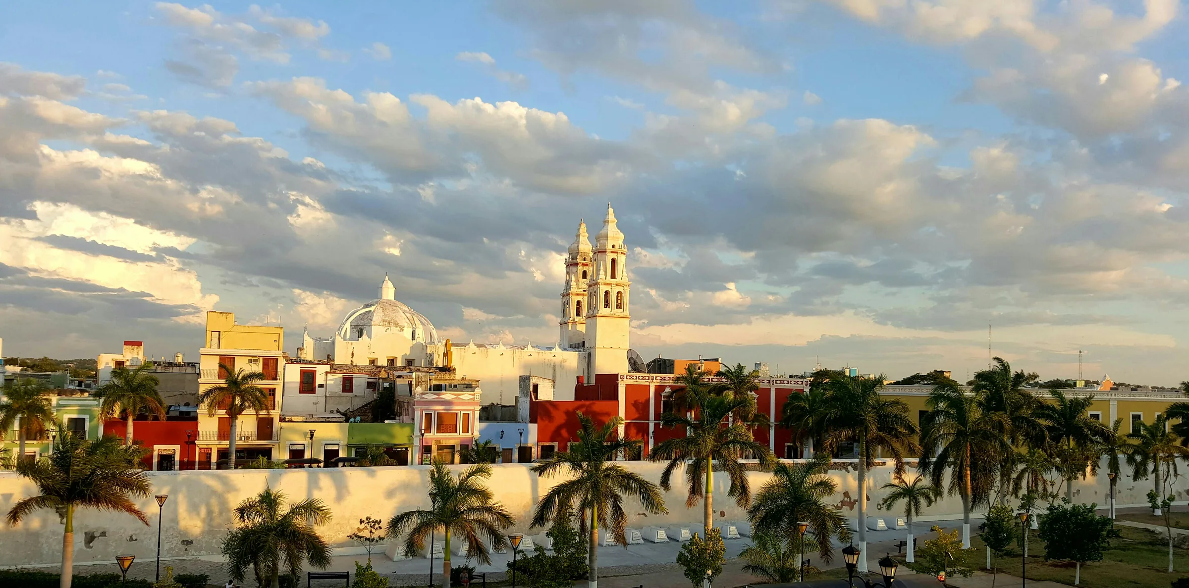 Vue du centre historique de Campeche avec les tours de la cathédrale, une coupole et des maisons colorées derrière une rangée de palmiers
