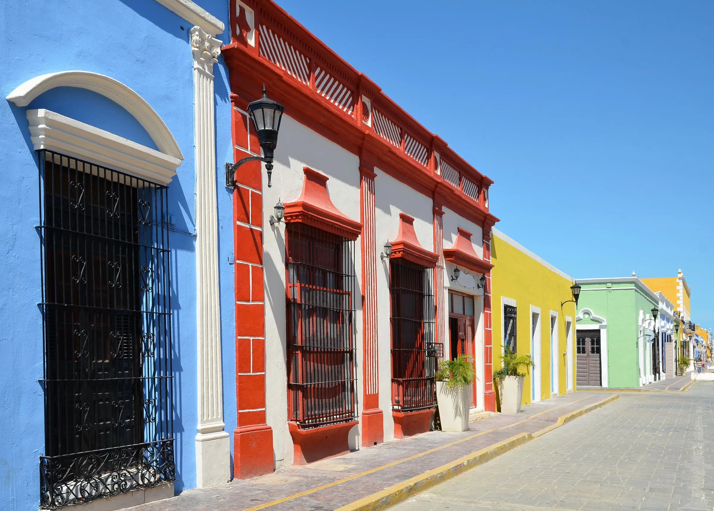 Fachadas azul y roja con ventanas enrejadas y faroles en una calle del centro histórico de Campeche
