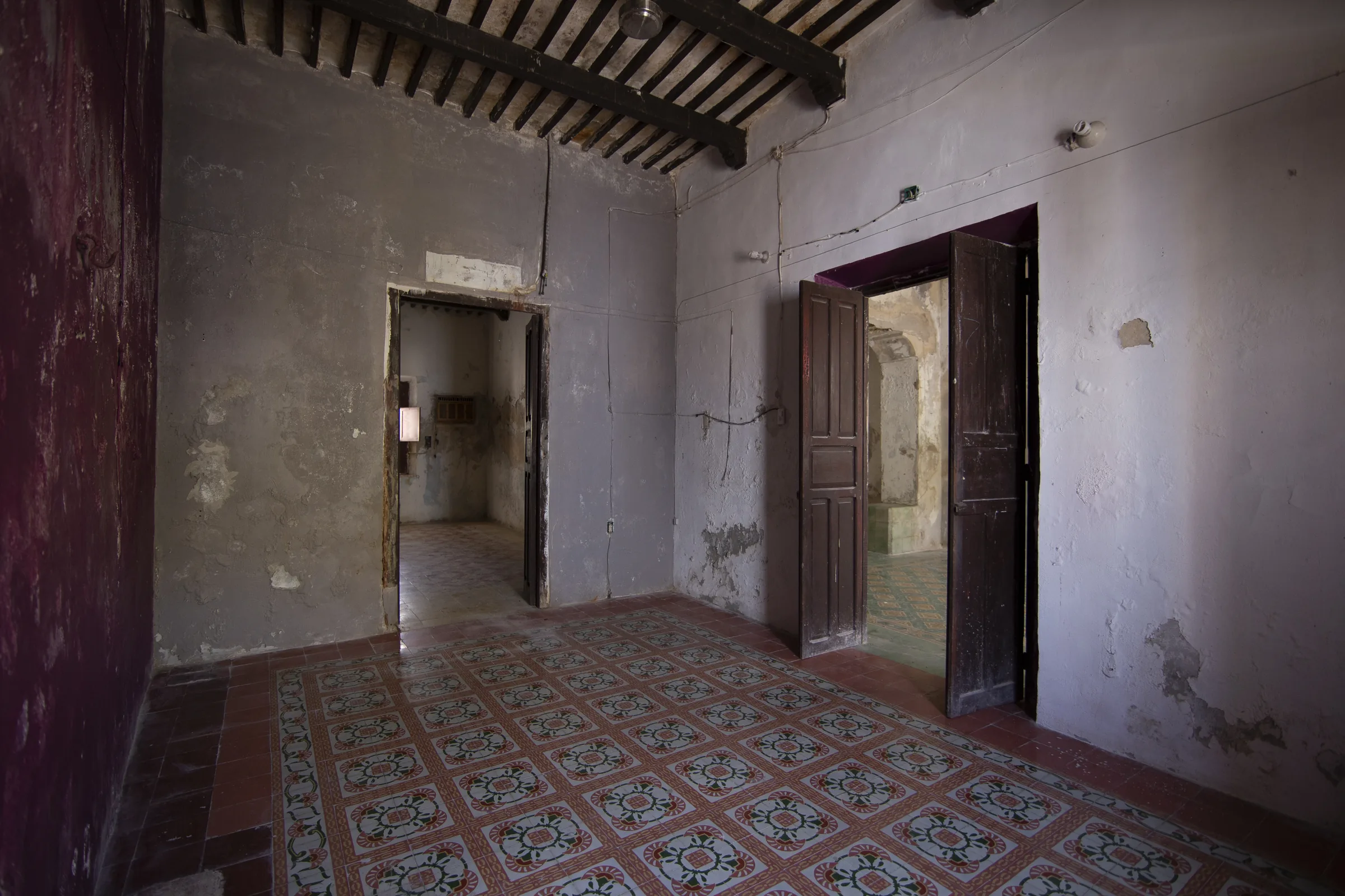 Chambre de La Casa Verde avant la restauration, avec plafond à poutres, sol en carreaux de ciment et portes en bois