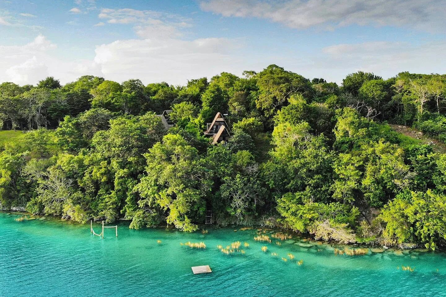 Aerial view of the A-frame cabins of Azul Nomeolvides in the forest above the turquoise shore of Bacalar lagoon