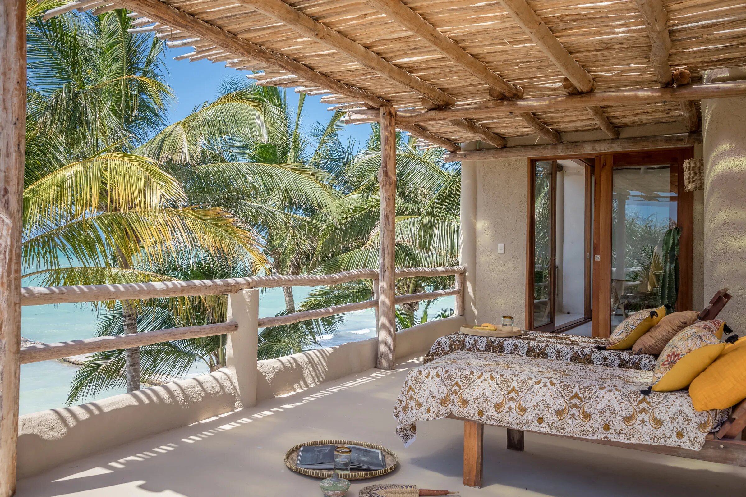 Covered terrace at Casa Cat Ba with two daybeds and yellow cushions, among palm trees facing the sea in Holbox
