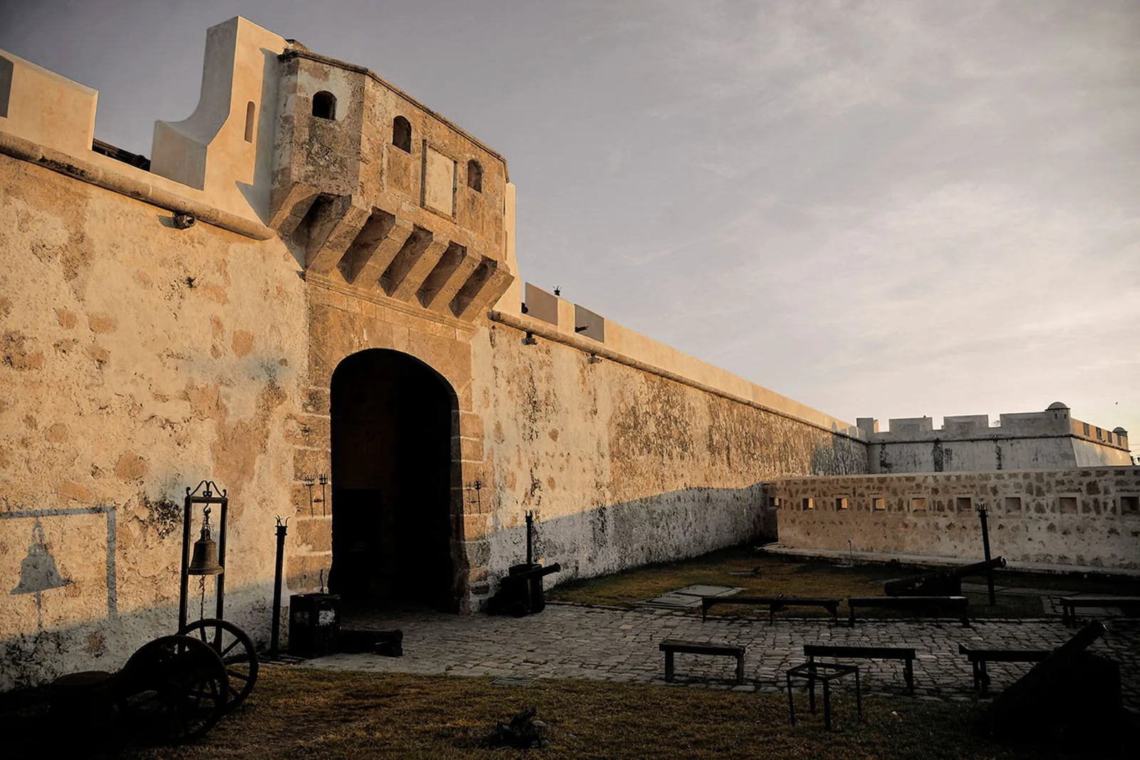 The Puerta de Tierra and Campeche's curtain wall at dusk, with cannons in the courtyard